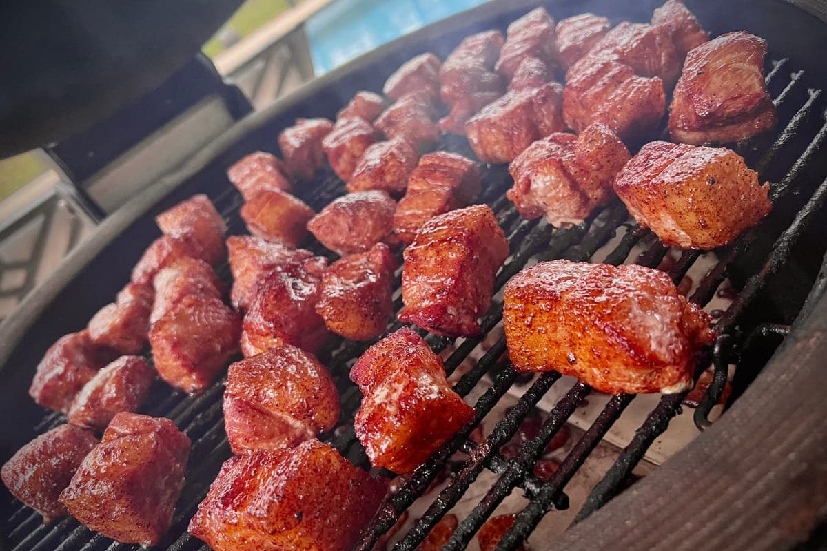 Cubes of smoked meat with a deep bark, lined up on a round grill grate